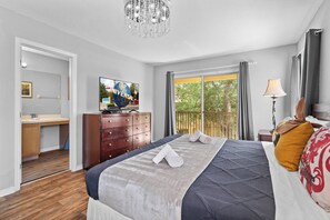 Habitación de hotel moderna con una cama grande, televisión, escritorio y balcón con vistas a árboles.