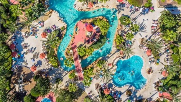 An aerial view of a resort with multiple swimming pools, sun loungers, and palm trees.