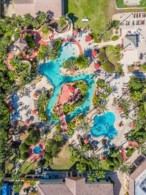 Vista aérea de un complejo turístico con varias piscinas, tumbonas y palmeras.