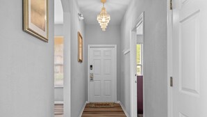 A hallway with a wooden floor, a white door, and a chandelier.