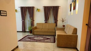 Un salón con un sofá color beige, un tapete estampado y cortinas.