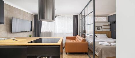 Una habitación de hotel moderna con área de cocina, sofá, cama y un amplio ventanal.