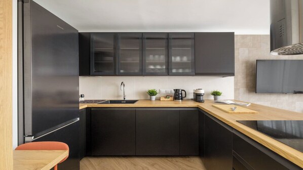 A modern kitchen with black cabinets, a wooden countertop, a sink, a coffee maker, and a small plant. - Sun & Snow Graniczna (Warsaw)
