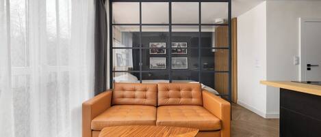 A modern living room with a leather sofa, a wooden coffee table, and a glass partition with framed pictures.