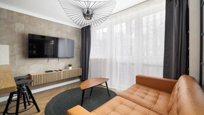 Ett modernt vardagsrum med en stor TV, en träbänk, en soffa och en matplats med ett bord och stolar.