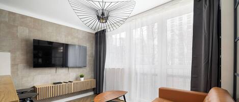 Una sala moderna con televisor grande, un banco de madera, un sofá y un comedor con mesa y sillas.