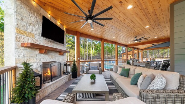 Eine Terrasse im Freien mit Kamin aus Stein, Deckenventilator und einer Sitzecke mit Sofa und Couchtisch.