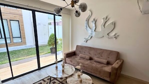 A spacious living room with a large window, a modern sofa, a chandelier, and decorative wall art. - Chipipe House, Salinas (Salinas)