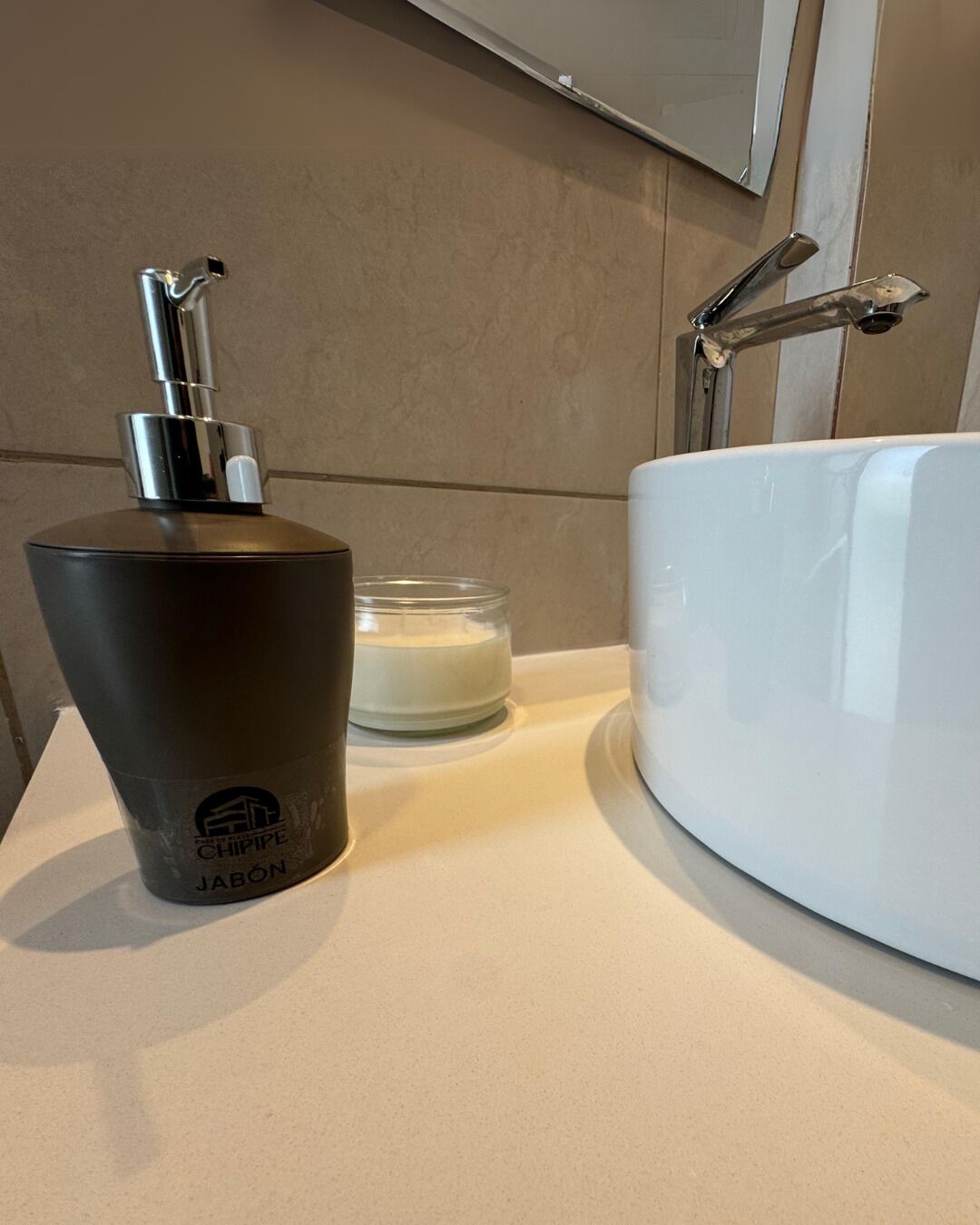 A bathroom with a white sink, a black soap dispenser, and a clear glass candle.