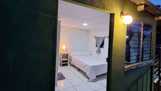 Una habitación con una cama, una mesita de noche, una lámpara y un ventanal con cortinas.