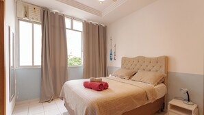 A neatly arranged bedroom with a large bed, a bedside table, and a window with curtains.