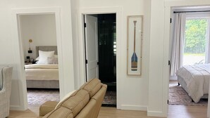Amplia sala de estar con sofá color beige, cama con ropa blanca y una pala enmarcada en el pasillo.