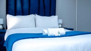 A neatly made bed with white and blue bedding, a blue headboard, and a folded towel on the bed. - LUGOGO GUESTHOUSE (Thohoyandou)