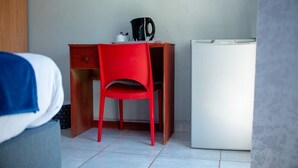 A small room with a wooden desk, a red chair, a white refrigerator, and a bed with a blue blanket. - LUGOGO GUESTHOUSE (Thohoyandou)