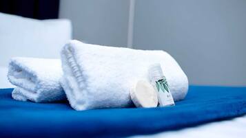A neatly folded white towel and a bottle of hand soap on a blue surface, likely a bed or a table.