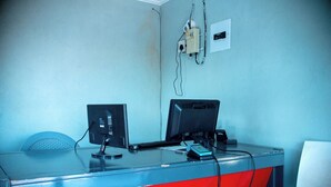 A desk with two monitors, a keyboard, and a mouse. There is a wall socket and a power strip on the wall. - LUGOGO GUESTHOUSE (Thohoyandou)