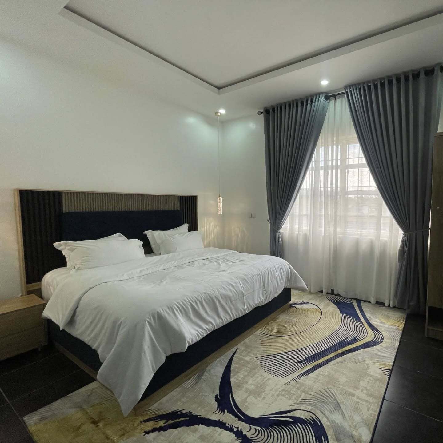 Une chambre moderne avec un grand lit, une tête de lit, une fenêtre avec des rideaux et un tapis à motifs.