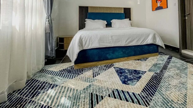 A modern hotel room with a large bed, a patterned rug, and a painting on the wall. - Lekosokky  Hotel and Suites (Ijoko)