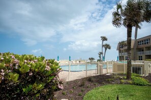 A pool area with a fence, palm trees, and a building in the background.