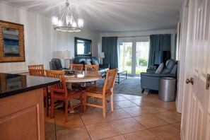 A dining area with a round table and chairs, a sofa, a TV, and a view of the outdoors.
