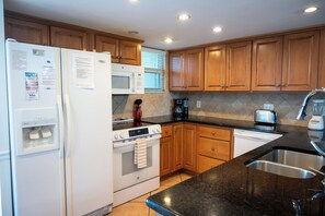 A kitchen with wooden cabinets, a white refrigerator, a stove, a dishwasher, and a sink.