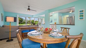 Un coin repas avec une table ronde en bois, des chaises rembourrées bleues et un ventilateur de plafond.