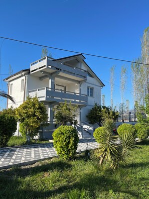 A two-story residential building with a balcony, surrounded by greenery and a paved walkway. - Elodi’s Villa (Fushkruje)