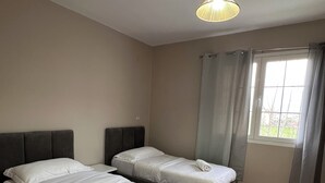 A room with two beds, a round rug, a window with curtains, and a hanging light fixture. - Elodi’s Villa (Fushkruje)