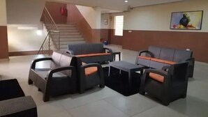 Un vestíbulo con una escalera, zona de estar con sofás y mesas, y una pared con una pintura de frutas.