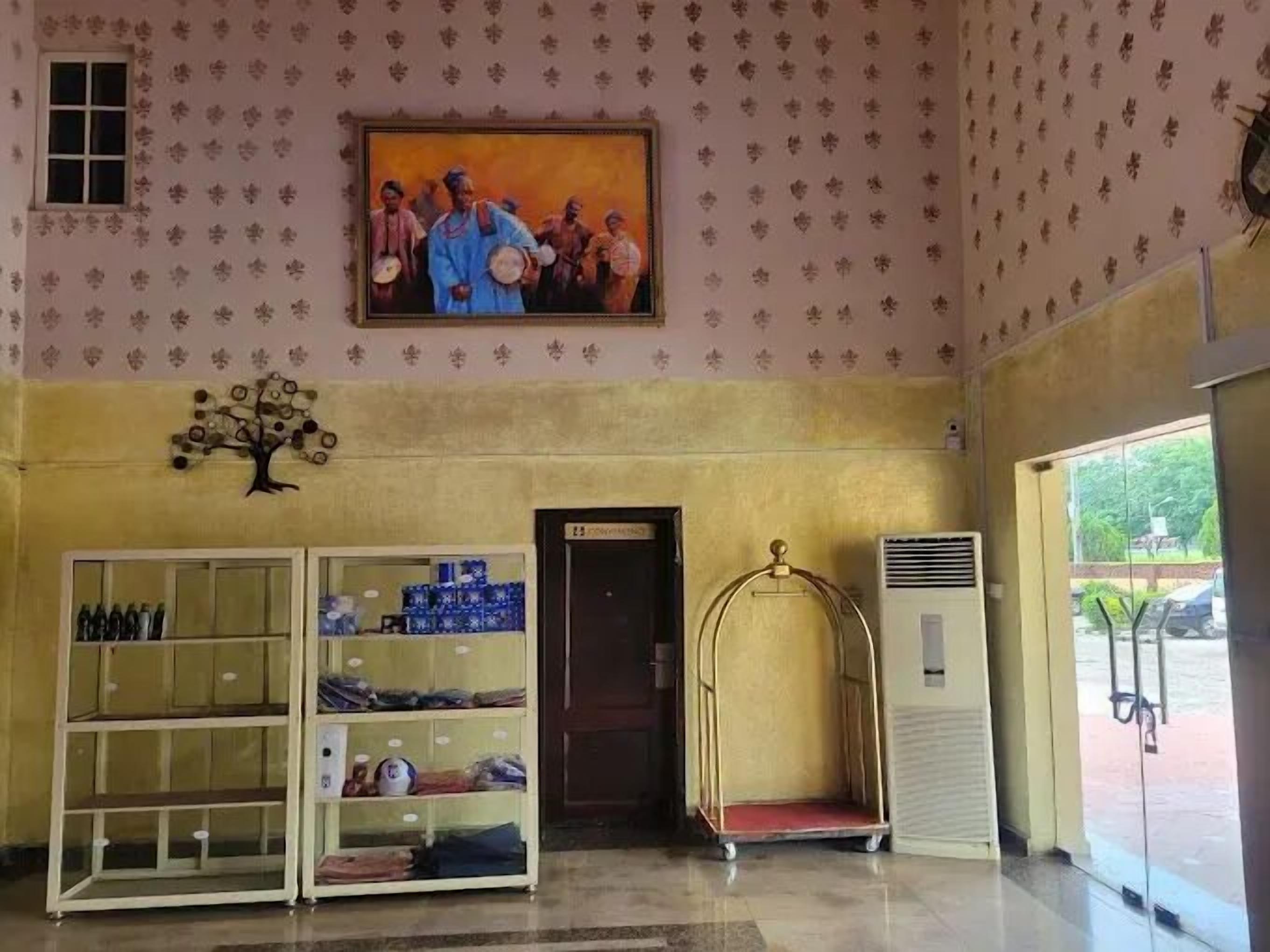 A lobby with patterned wallpaper, a painting, a tree decoration, a vending machine, and a metal chair.