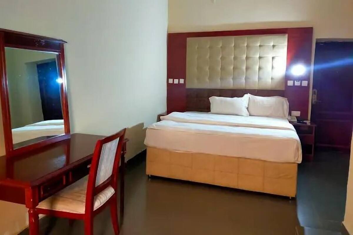 Una habitación de hotel con cama, escritorio, silla y espejo.