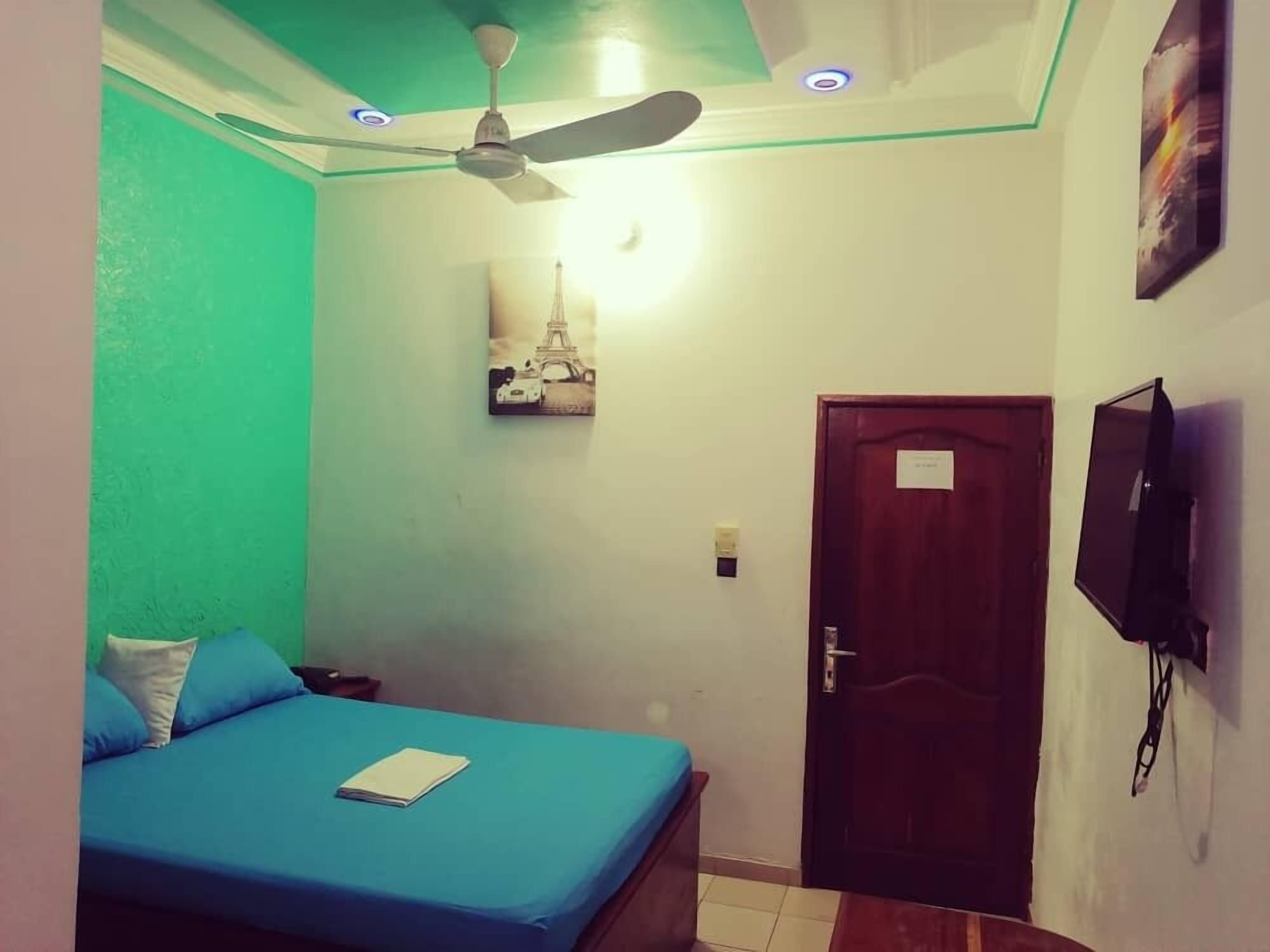 A bedroom with a bed, a ceiling fan, a door, and a wall-mounted TV.
