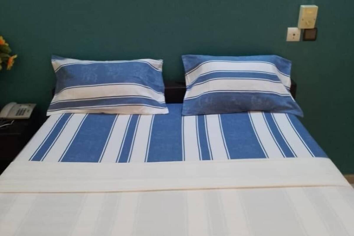 Ein Bett mit gestreifter Bettwäsche und zwei Kissen, ein Nachttischtelefon und eine Steckdose.