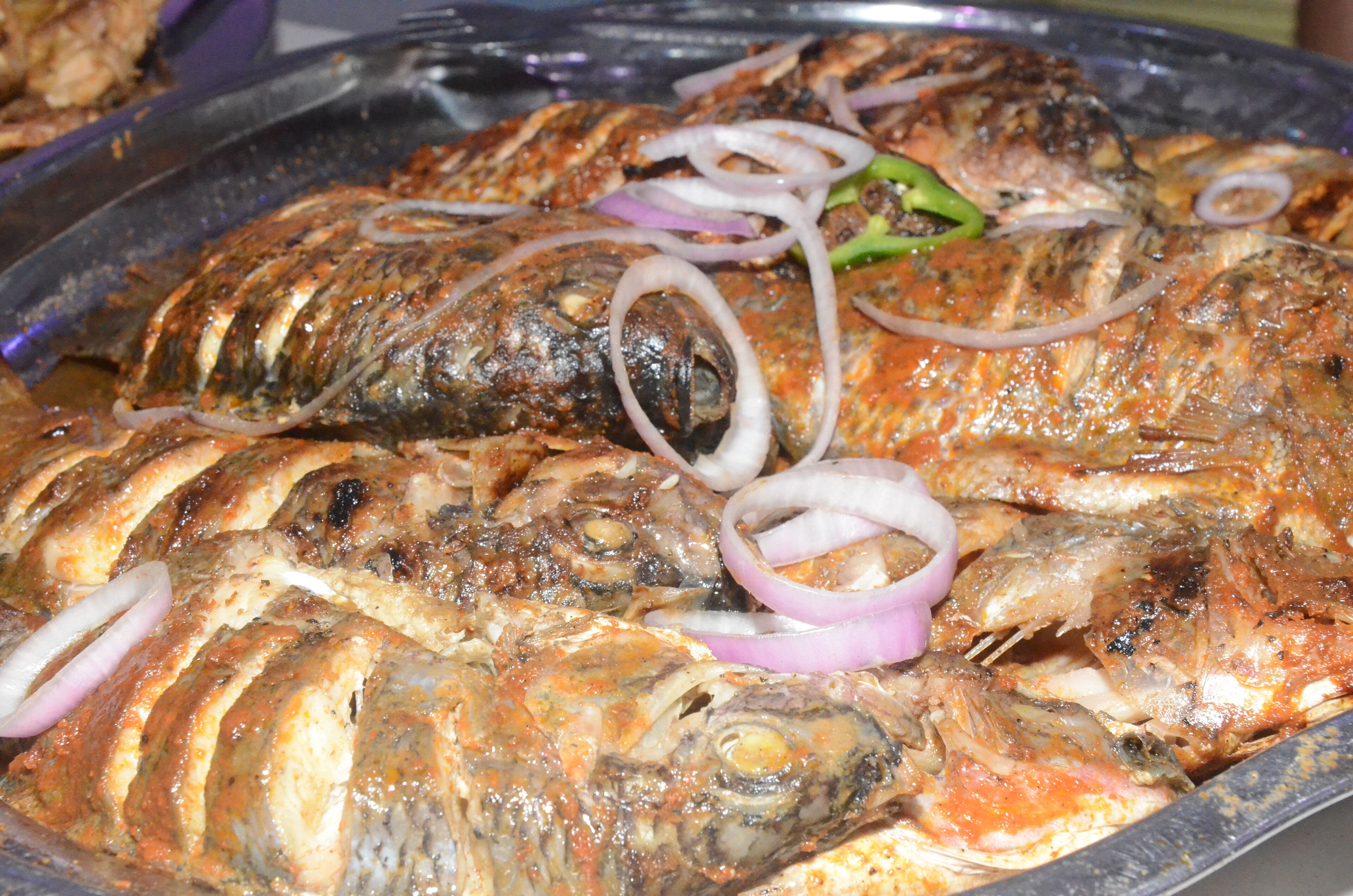 A large tray of grilled fish with sliced onions and green peppers.