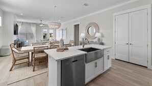 A modern kitchen with a central island, stainless steel sink, and white cabinetry. - Sugar Shores at Summer Salt (Orange Beach)