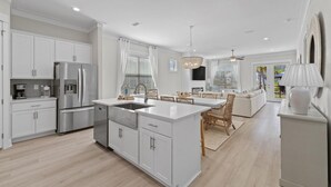 A modern kitchen with white cabinetry, a stainless steel refrigerator, and a central island with a sink. - Sugar Shores at Summer Salt (Orange Beach)