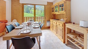 Un comedor con una mesa de madera dispuesta para cuatro personas, sillas y vistas a un paisaje verde a través de amplios ventanales.