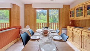 Un comedor con una mesa de madera dispuesta para cuatro personas, ventanas amplias que ofrecen vistas a un paisaje verde y armarios de madera con puertas de vidrio.