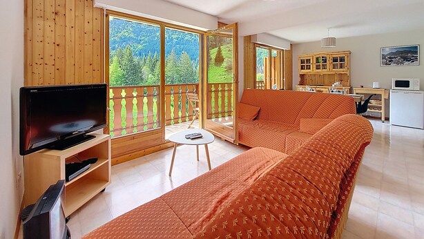 Una sala de estar con un sofá grande, un televisor y un balcón con barandillas de madera.