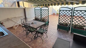 An outdoor patio with a round table and chairs, surrounded by potted plants and a covered area with a striped awning. - Independent apartments with fully equipped kitchen in central location (Lipari)