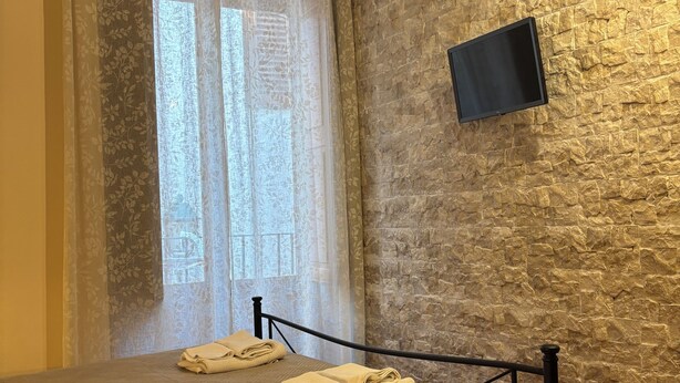 A bedroom with a bed, a mounted TV, and a stone-textured wall. - Independent apartments with fully equipped kitchen in central location (Lipari)
