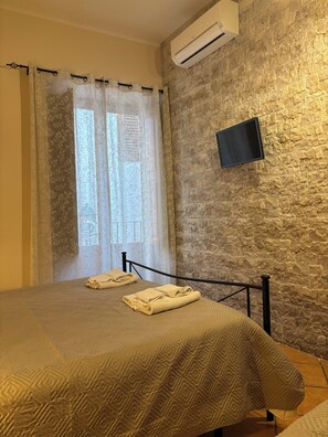 A bedroom with a bed, a mounted TV, and a stone-textured wall. - Independent apartments with fully equipped kitchen in central location (Lipari)