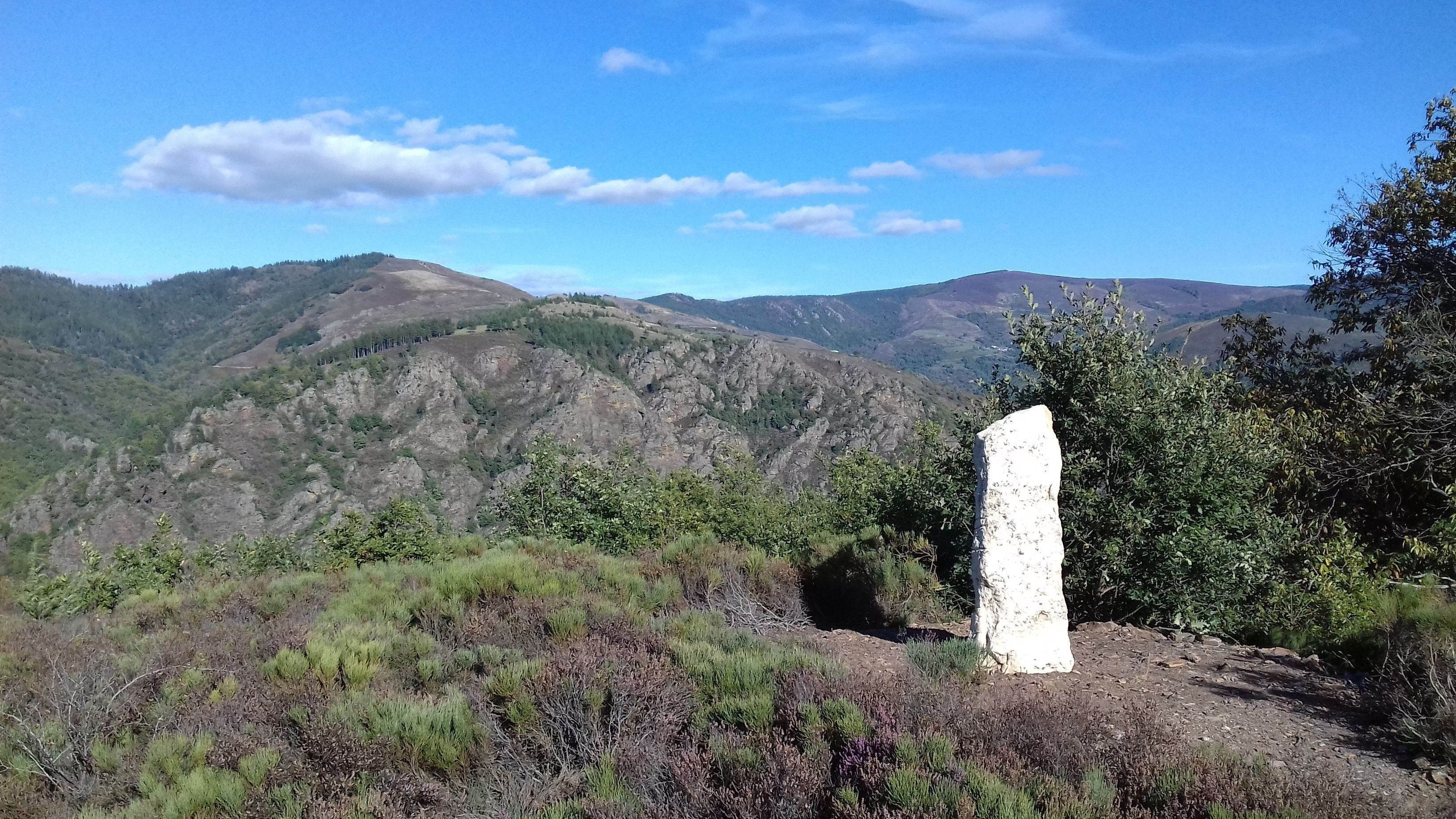 A natural landscape with a prominent white rock formation in the foreground, surrounded by greenery and hills in the background.