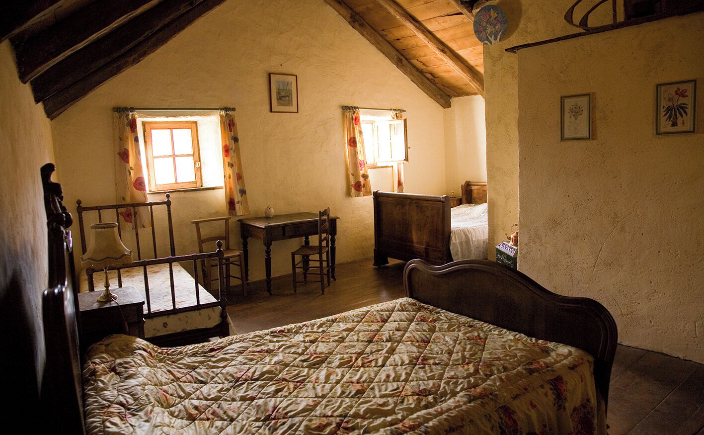 Un dormitorio con una cama, un escritorio y dos ventanas con cortinas.