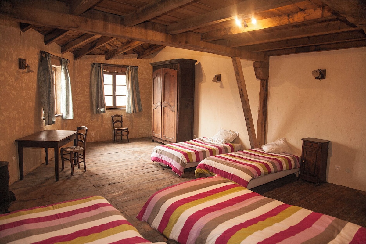 Una habitación rústica con vigas de madera, un escritorio, dos camas con ropa de cama a rayas y una silla.