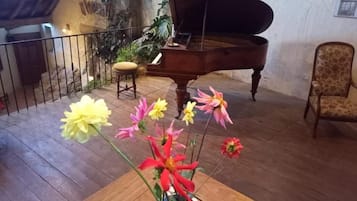 Un piano de cola en una habitación con piso de madera, una planta en maceta con flores y una silla.