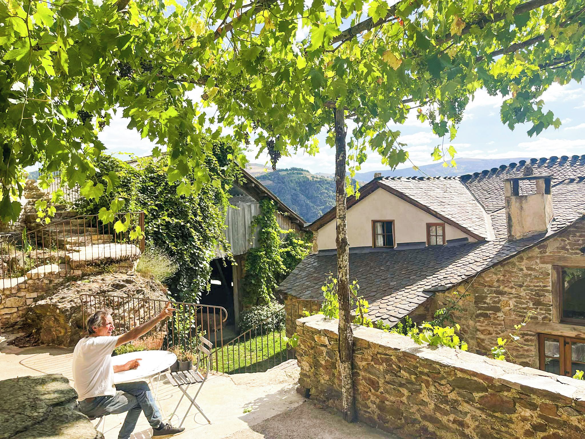 A stone house with a tiled roof, a stone wall, and a view of the countryside.
