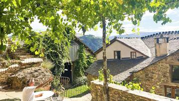 A stone house with a tiled roof, a stone wall, and a view of the countryside.