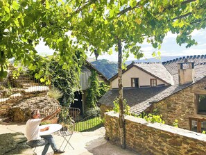 A stone house with a tiled roof, a stone wall, and a view of the countryside.