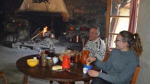 Un interior rústico con chimenea de piedra, vigas de madera y una mesa dispuesta para una comida.
